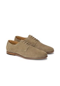 Chaussures de ville en daim beige avec une texture lisse, un bout rond et cinq œillets pour les lacets. Elles présentent une semelle fine marron pour un aspect élancé.
