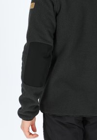 Pullover in pile grigio scuro con toppe in tessuto nero sui gomiti. Presenta un orlo rotondo e una superficie testurizzata, che offrono calore e comfort.