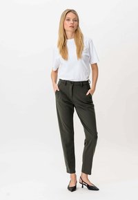 Biała koszulka z krótkim rękawem w połączeniu z ciemnozielonymi spodniami o dopasowanym kroju, które mają boczne kieszenie. Model ma na sobie czarne buty na obcasie. Prosty, nowoczesny design.