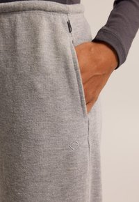 Pantalons de survêtement à côtes gris clair en tissu doux, avec une poche latérale et un petit logo brodé sur la hanche.