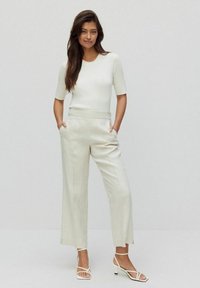 Witte ribgebreide top met korte mouwen, gecombineerd met lichtbeige wijde broek met hoge taille. Accessoires zijn strappy witte sandalen.