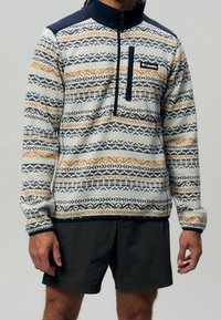 Pull-over Columbia en écru, marine et orange, présentant un motif géométrique, une fermeture éclair au quart et une poche poitrine avec logo.