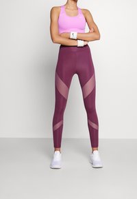 Dopasowany różowy top sportowy; legginsy w kolorze burgundowym z wysokim stanem i siateczkowymi panelami; białe trampki; opaski na nadgarstki; bezszwowy, sportowy design.