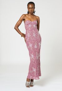 Trägerloses pinkes Abendkleid mit kunstvollen Perlen und Blumenmustern; figurbetonte Silhouette mit leichtem Auslauf am Saum; getragen mit silbernen Absätzen.