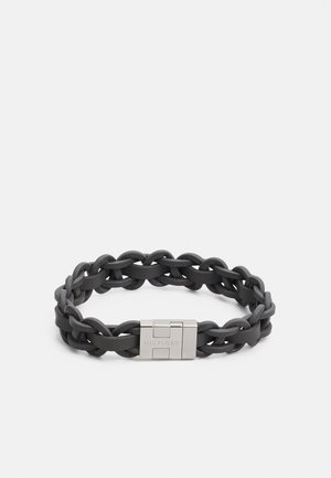 Bracelet en cuir tressé noir avec fermoir en métal argenté gravé de "HILFIGER" sur un fond blanc.