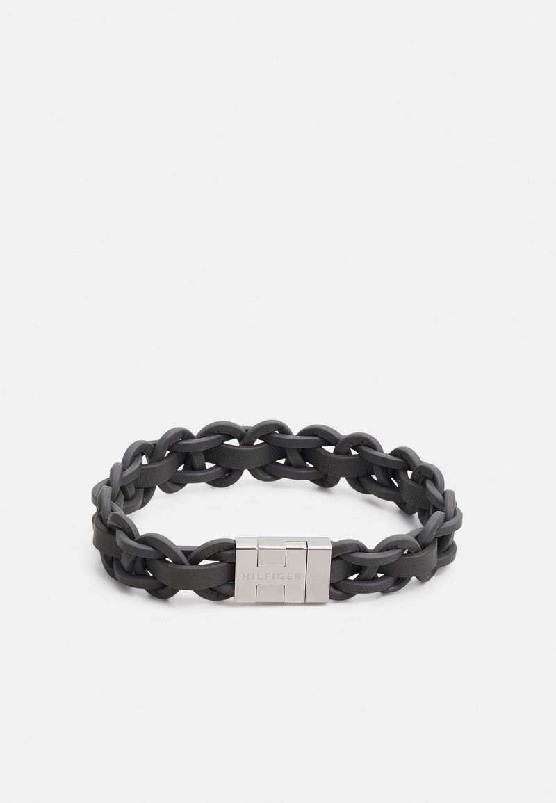 Bracelet en cuir tressé noir avec fermoir en métal argenté gravé de "HILFIGER" sur un fond blanc.