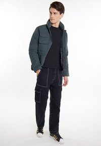 Mørkegrøn polstret jakke med høj krave, fire forreste lommer, parret med sorte cargo bukser med hvide syninger og sneakers.