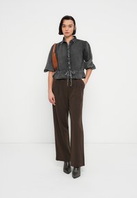 Γκρι μπλούζα με κοντά μανίκια και ρυθμιζόμενο κορδόνι στη μέση, συνδυασμένη με καφέ παντελόνια ψηλόμεσα και μαύρα μποτάκια αστραγάλου. Απλός, μοντέρνος σχεδιασμός.