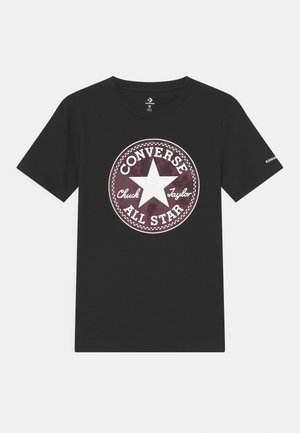 Camiseta negra de manga corta con un gran logotipo circular de Converse All Star que presenta una estrella blanca y la inscripción "Chuck Taylor" en la parte delantera.