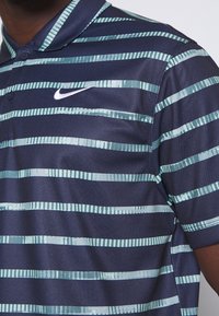 Polo bleu marine avec des rayures horizontales en vert clair et turquoise. Le tissu a un aspect texturé avec un col à boutons.