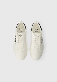 Valge paar Armani Exchange'i tennisetossusid mustade triipudega ja mustade kandmisaktsentidega, vaadatuna ülalt valgel taustal.