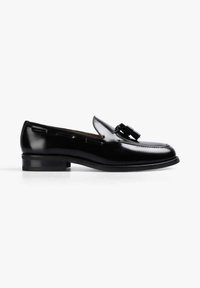 Mocasín de charol negro, con detalle de borlas, punta redondeada y tacón bajo apilado con costuras visibles a lo largo de los bordes.