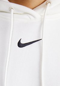 Sudadera blanca con el logo de Nike en forma de swoosh bordado en el pecho, mostrando el escote y los cordones.