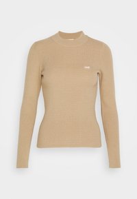 Pull à col roulé beige côtelé à manches longues avec un petit logo blanc sur la poitrine. Confectionné en tissu doux et texturé.
