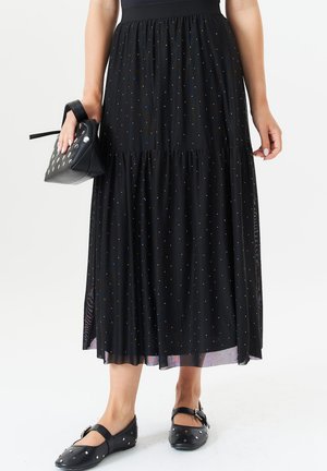 Black tiered maxi skirt with scattered silver dots, paired with a small black bag featuring circular hardware and black flat shoes.
