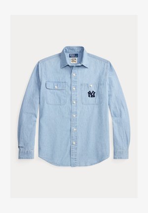 Svetlo modra denim srajca z gumbi na sprednji strani, dvema prsnikoma in vezenim mornarsko modrim logotipom NY na levem žepu. Dolgi rokavi z gumbi na manšetah.