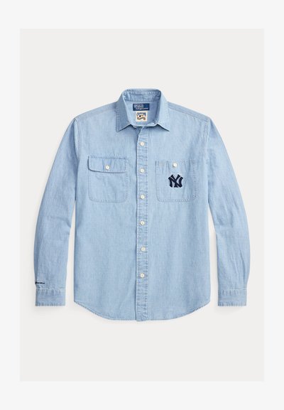 Svetlo modra denim srajca z gumbi na sprednji strani, dvema prsnikoma in vezenim mornarsko modrim logotipom NY na levem žepu. Dolgi rokavi z gumbi na manšetah.