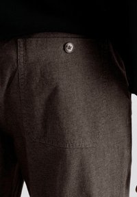 Pantalons bruns texturés avec un bouton visible sur la poche arrière, arborant un motif à carreaux subtil et une finition lisse.