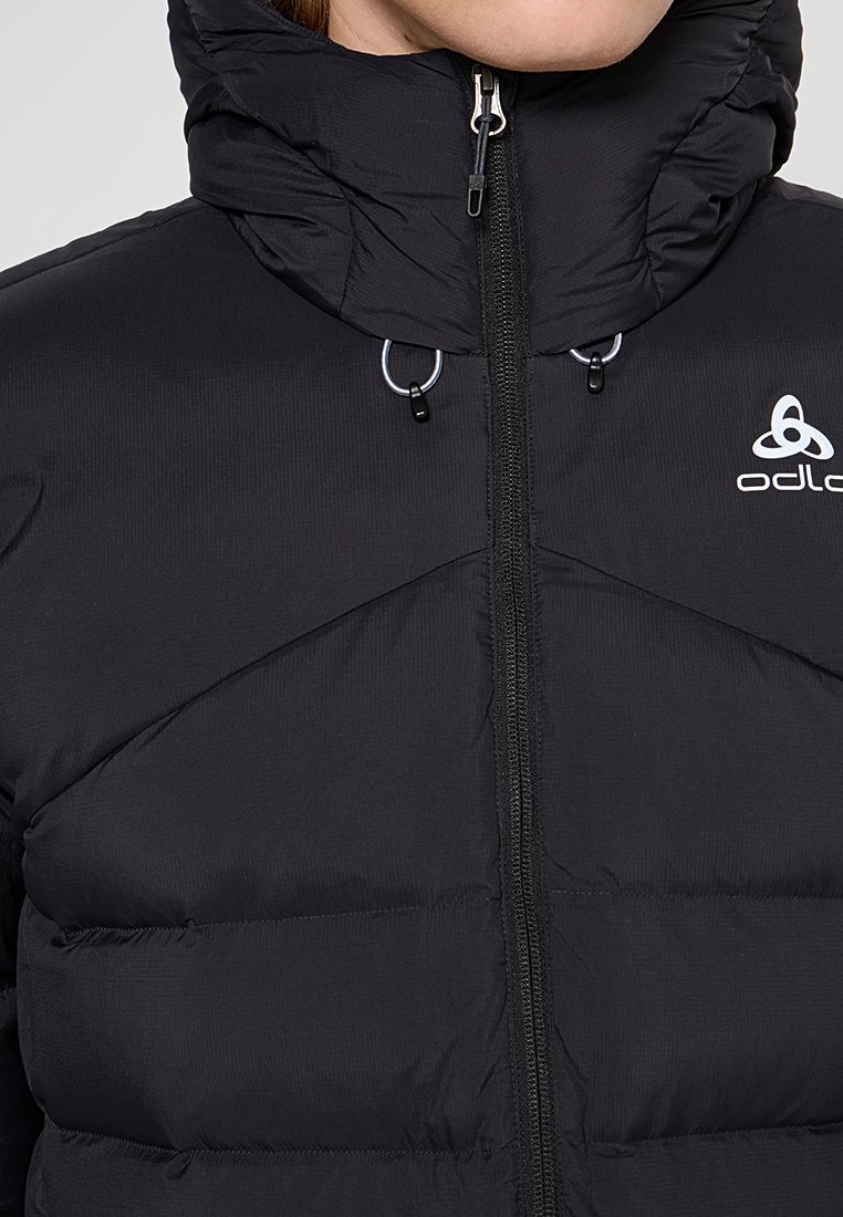 Nahaufnahme einer Person, die eine schwarze Odlo gepolsterte Jacke mit hohem Kragen und einem Reißverschluss vorne trägt.
