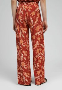 Pantalons larges à motifs rouges avec une taille élastique, motifs floraux et animaliers en orange et blanc, et une texture de tissu lisse.
