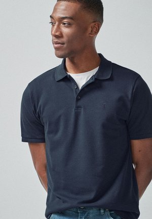Polo de color marino hecho de algodón con una textura suave, que cuenta con una tapeta de tres botones y un logo sutil en el pecho.