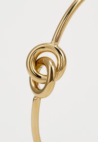 Gylden armbånd med sammenflettede sirkulære design, glatt overflate og glatt, polert finish. Enkelt og moderne i form.