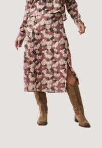 Falda midi floral en rosa empolvado con flores blancas y hojas verdes; presenta una abertura y se combina con botas de vaquero de ante marrón.