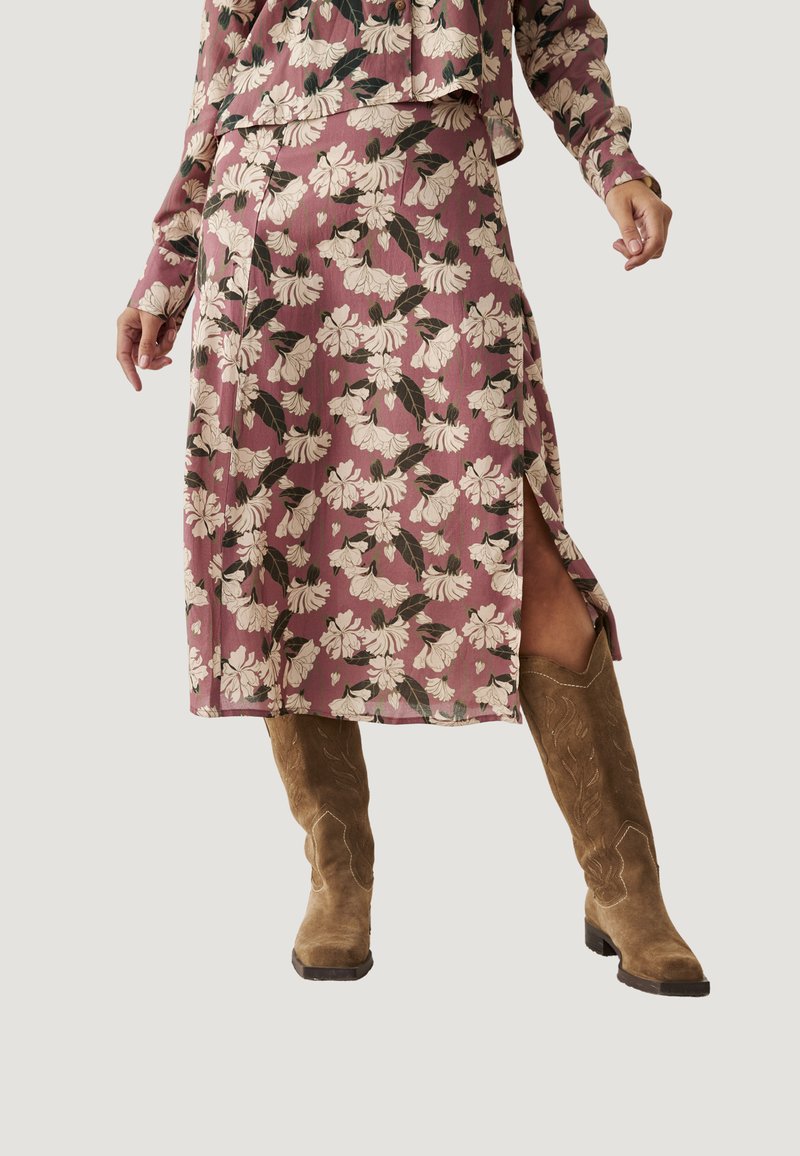Falda midi floral en rosa empolvado con flores blancas y hojas verdes; presenta una abertura y se combina con botas de vaquero de ante marrón.