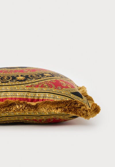 Plüss négyzet alakú párna piros, fekete és arany mintás anyagból, rojtos arany szegéllyel és sima textúrával.