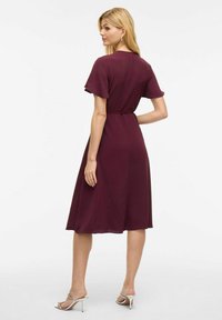 Vestido burdeos en corte A con mangas cortas, tejido texturizado y cintura ceñida. Presenta un dobladillo a la altura de la rodilla y un detalle mínimo.