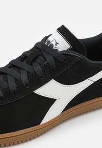 Sorte skinnesneakers med hvit lærdetalj, teksturert gummisåle og svarte lisser. Sølv logoetikett på tungen for merkevare.