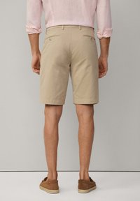 Beige Baumwollshorts mit Gesäßtaschen, flacher Vorderseite und geraden Beinen, kombiniert mit braunen Slippern. Minimalistisches Design und klare Linien.