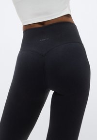 Κολάν μαύρα, με ψηλή μέση και ριμπ ζώνη, κατασκευασμένα από απαλό, ελαστικό ύφασμα με λείο, ελαφρώς γυαλιστερό φινίρισμα.