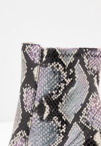 Ankelstövel med ett mönster av flerfärgad ormskinn, med texturerade fjäll och en glansig yta. Svarta, lila och subtila blå nyanser förekommer.