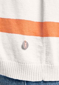 Gebreide trui met witte en oranje horizontale strepen. Beschikt over een ronde grijze label met een roze honden-silhouet. Zachte textuur, ribbelrand.
