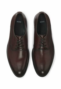 Scarpe eleganti in pelle marrone con una texture liscia, caratterizzate da una punta arrotondata, sei passanti per i lacci e una suola in gomma nera.