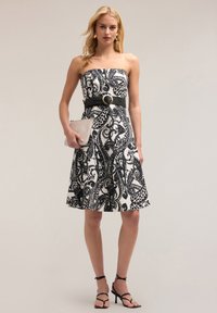 Rochie fără bretele, alb-negru, cu un model paisley, curea neagră strânsă cu o cataramă circulară și fustă evazată până la genunchi.