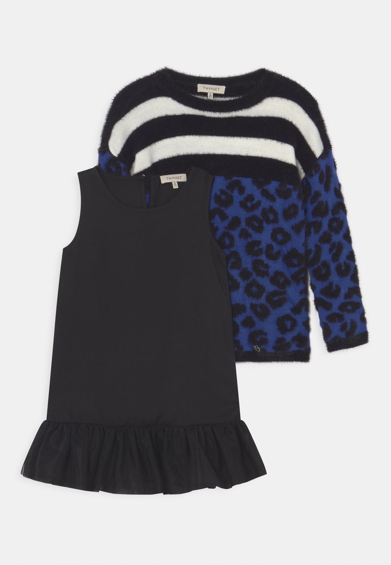 Robe noire sans manches avec un ourlet volanté, associée à un pull duveteux avec des rayures noirs et blancs et un imprimé léopard bleu.