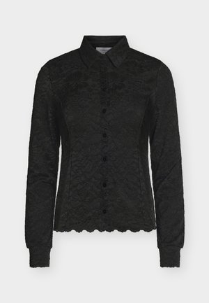 Melnā mežģīņu blūze ar garām piedurknēm, apkakli, pogas priekšpusē un viļņotu apakšu un aprocēm.