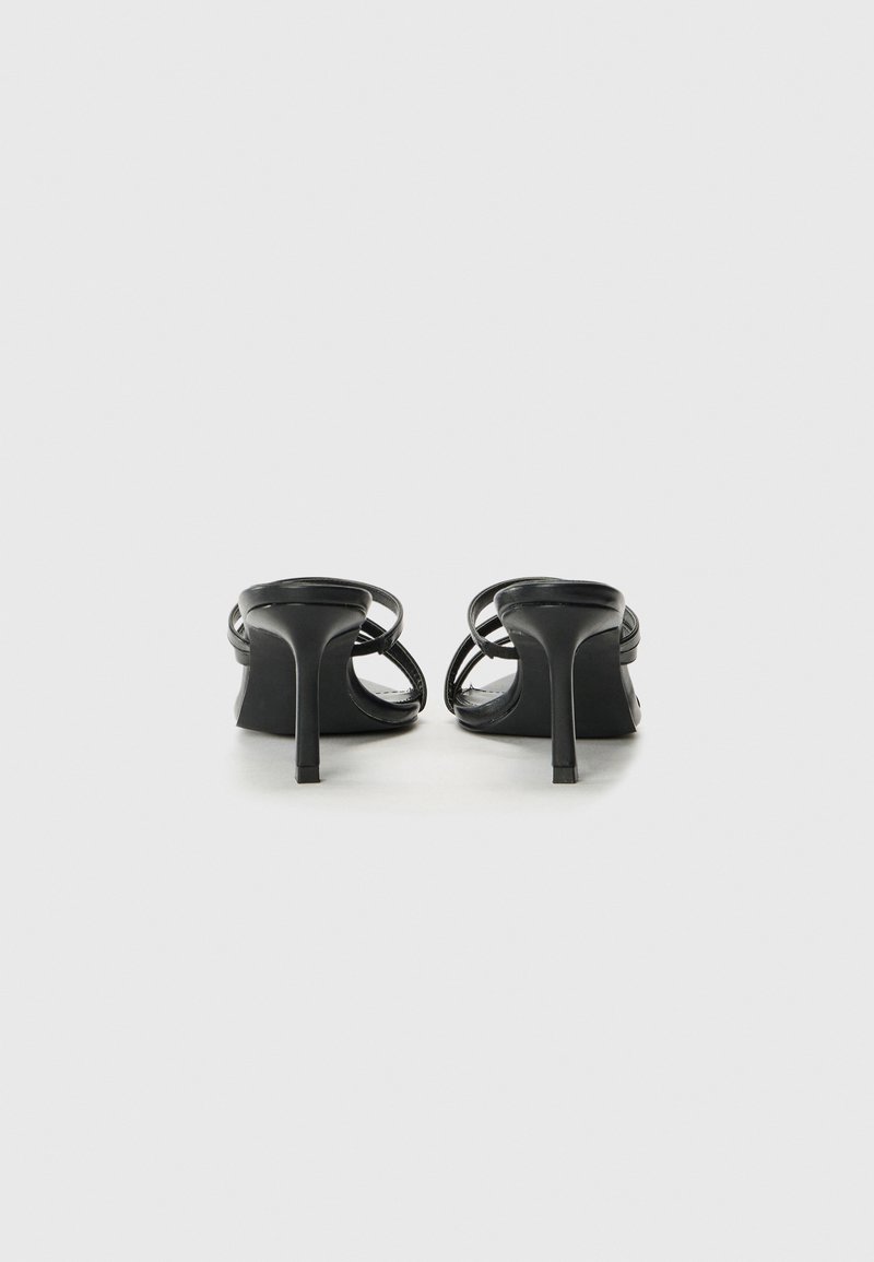 Sandales à talons hauts noires au design épuré, avec des fines brides croisées et un talon aiguille effilé. Fini en cuir lisse.