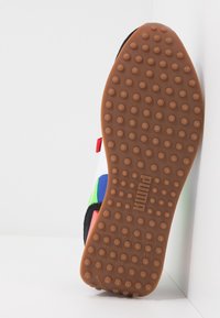 Semelle de chaussure Puma présentant une surface en caoutchouc marron texturée avec des motifs circulaires, rehaussée de sections supérieures noires, rouges, bleues, vertes et blanches.