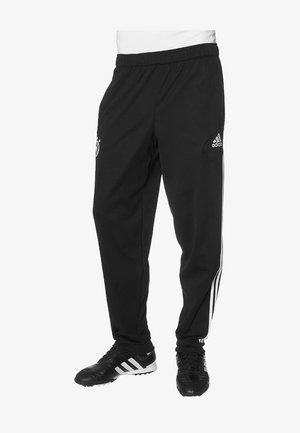 Zwarte Adidas trainingsbroek met witte zijstrepen en logo, gedragen met zwarte Adidas voetbalschoenen.