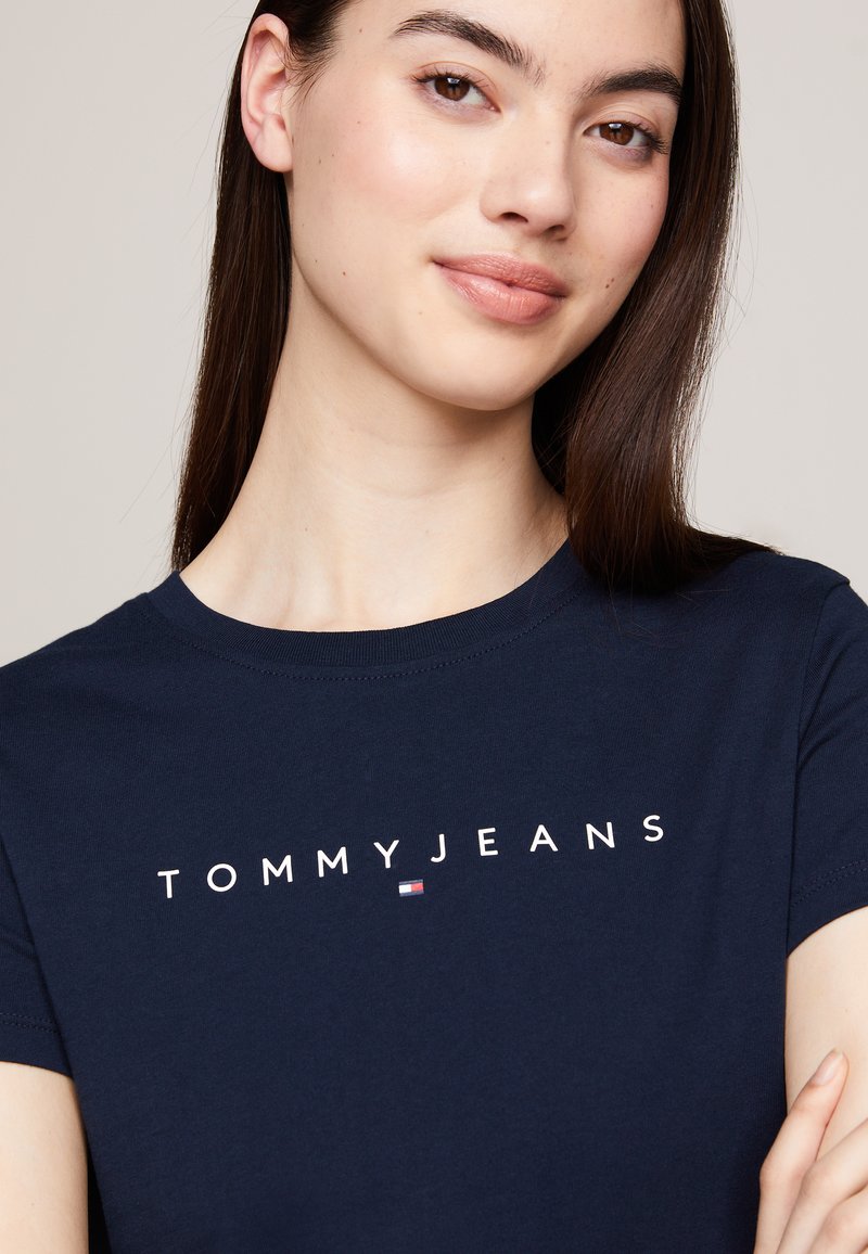 Camiseta de algodón de color azul marino con el texto "TOMMYJEANS" en blanco, cuello redondo, mangas cortas y un pequeño logo en el lado izquierdo.
