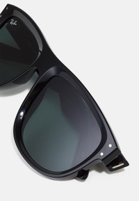 Ochelari de soare din plastic negru cu lentile întunecate, având o formă pătrată masivă, accente metalice și logo-ul Ray-Ban pe lentilă.
