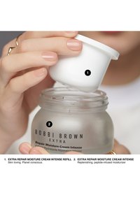 Bocal en verre dépoli avec un couvercle blanc, contenant une crème étiquetée "Bobbi Brown Extra Repair Moisture Cream Intense," avec une police de style manuscrit.