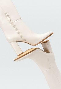 Weiße Lederstiefeletten mit einem quadratischen Absatz, ausgestattet mit einem seitlichen Reißverschluss und glatter Textur, die ein minimalistisches Design präsentieren.