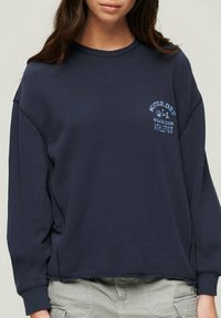 Felpa in cotone blu navy con vestibilità rilassata, scollatura rotonda e maniche lunghe. Presenta un logo blu chiaro sul petto e un orlo cropped.
