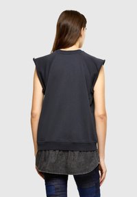 Sleeveless black sweatshirt with a ribbed texture, rounded neckline, and an extended hem, layered over a dark denim shirt.