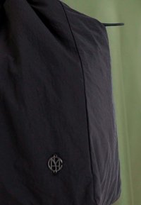 Schwarzer, leichter Stoff mit strukturiertem Finish; verfügt über ein kleines silbernes Logo an der Vorderseite und ein schlankes, minimalistisches Design.