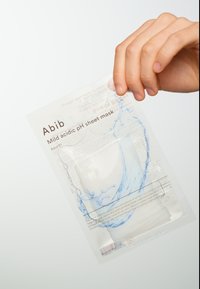 Emballage de masque en feuille en plastique transparent avec un design de éclaboussures d'eau blanches et bleues, étiqueté "Masque en feuille au pH acide doux" par Abib.
